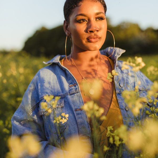 woman wearing blue denim jacket standing in flower field during daytime