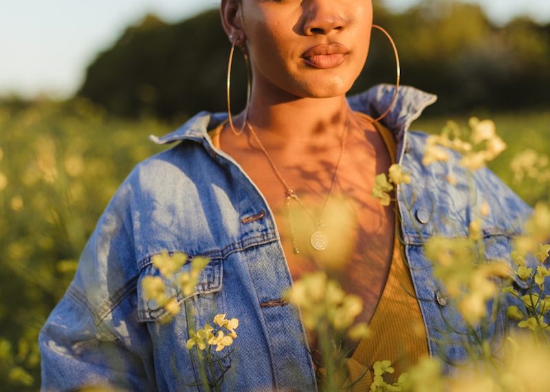 woman wearing blue denim jacket standing in flower field during daytime