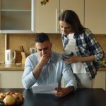 Couple looking stressed over bills at kitchen table.
