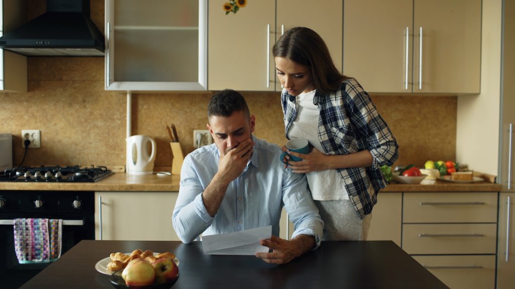 Couple looking stressed over bills at kitchen table.