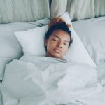 A young woman sleeping peacefully in a white bed.