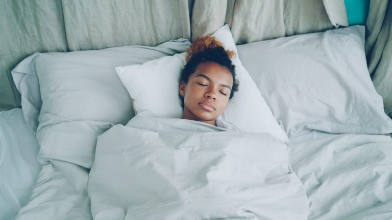 A young woman sleeping peacefully in a white bed.