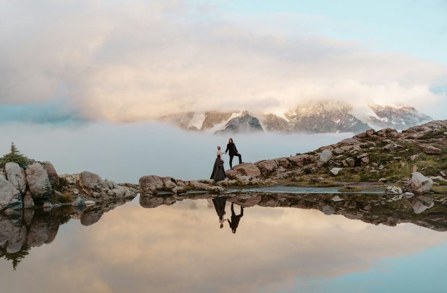 Couple standing on rocks by calm mountain lake reflection
