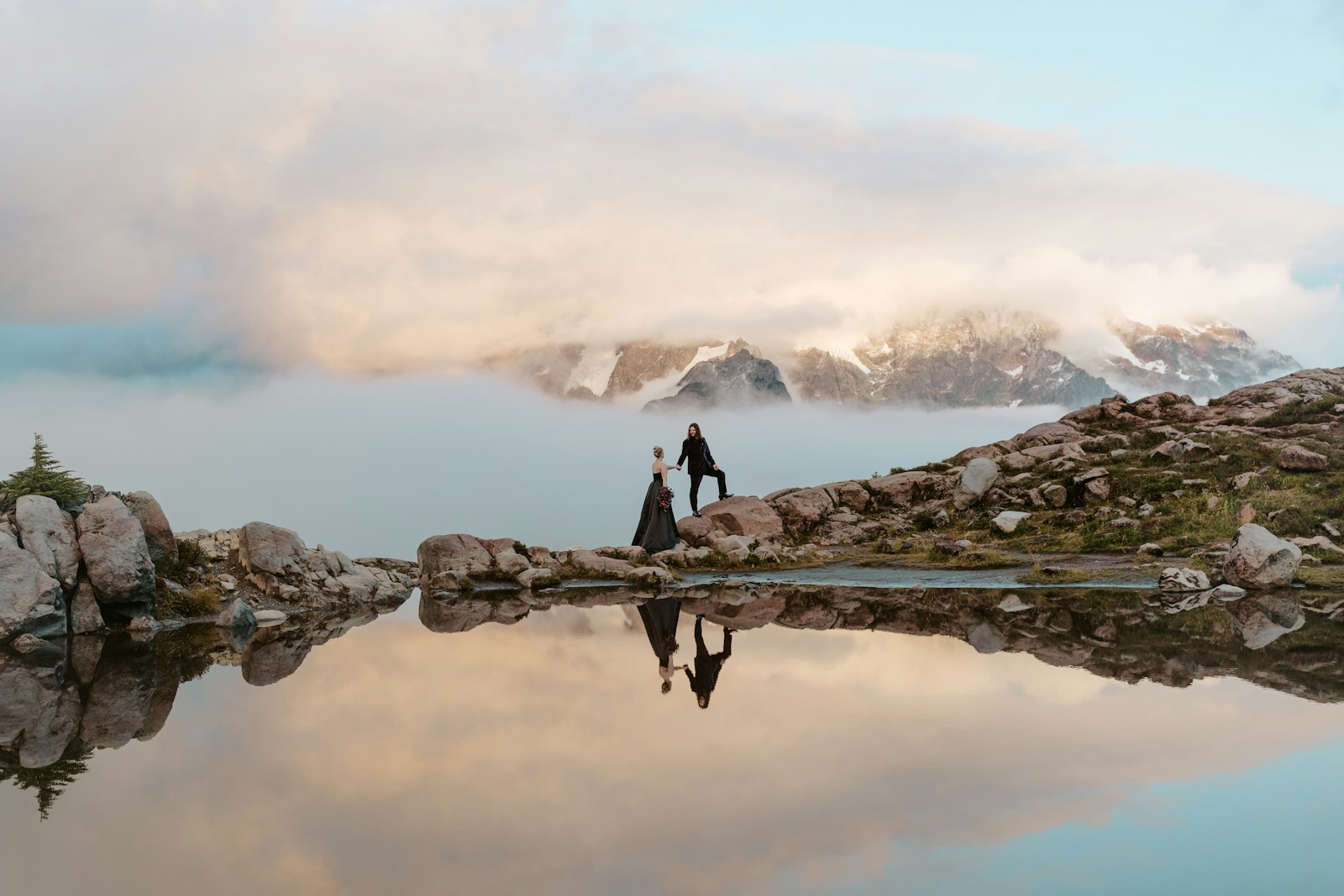 Couple standing on rocks by calm mountain lake reflection