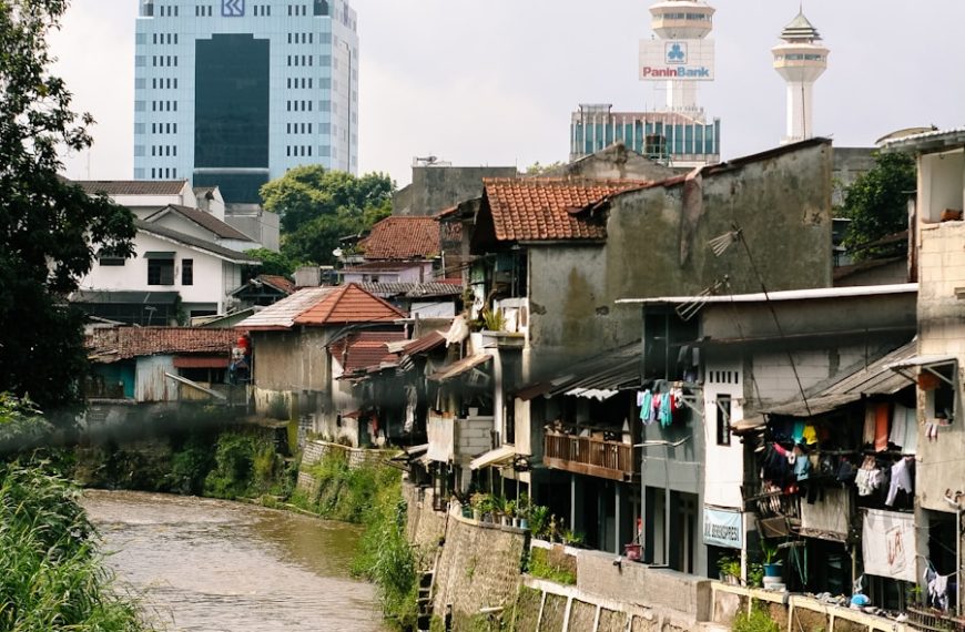 River flows past urban homes and modern buildings.
