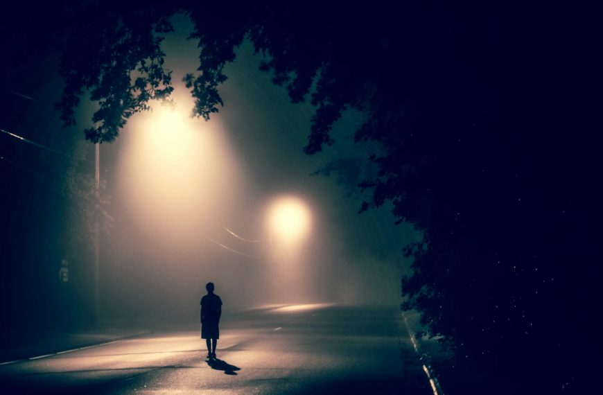silhouette of person standing on concrete road with streetlights turned on during nighttime